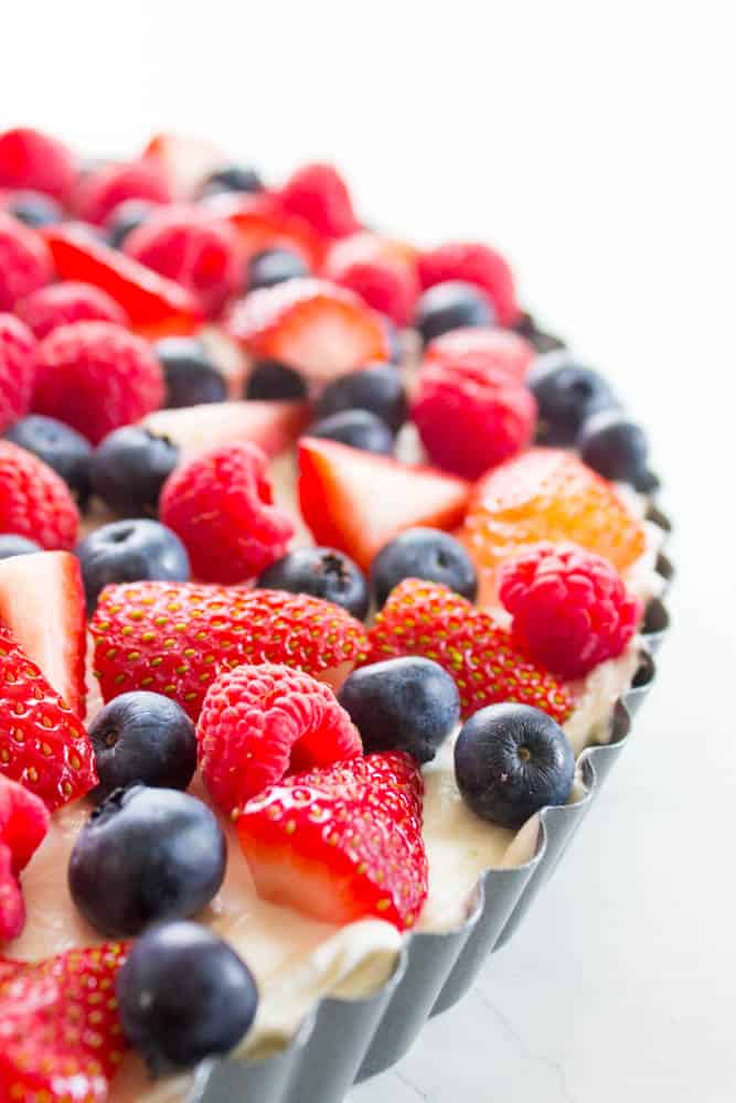 Insanely delicious & easy this Simple No-Bake Fruit Tart is made with an almond graham cracker crust, cream cheese filling, then topped with fresh fruit. Simple Fruit Tart in pan with strawberries, blueberries and raspberries