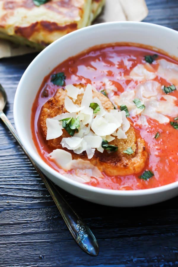 20-MINUTE CREAMY TOMATO BASIL SOUP is a classic comfort food and the is best tomato soup, thanks to 2 secret ingredients. tomato soup topped with cheese and toasted bread served in a white bowl
