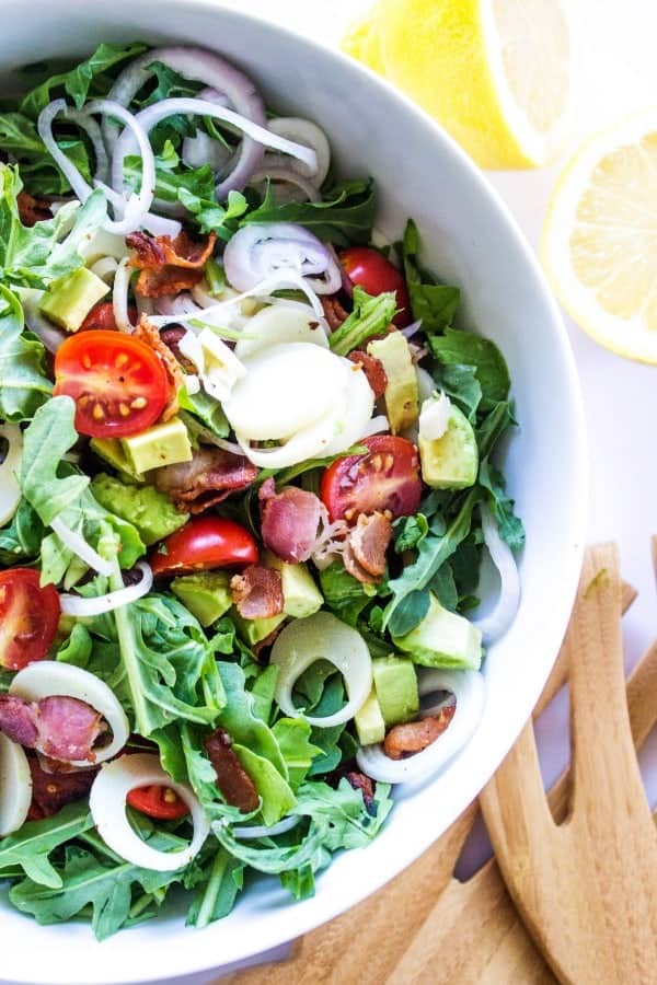 arugula and hearts of palm salad in white bowl with wooden salad spoons