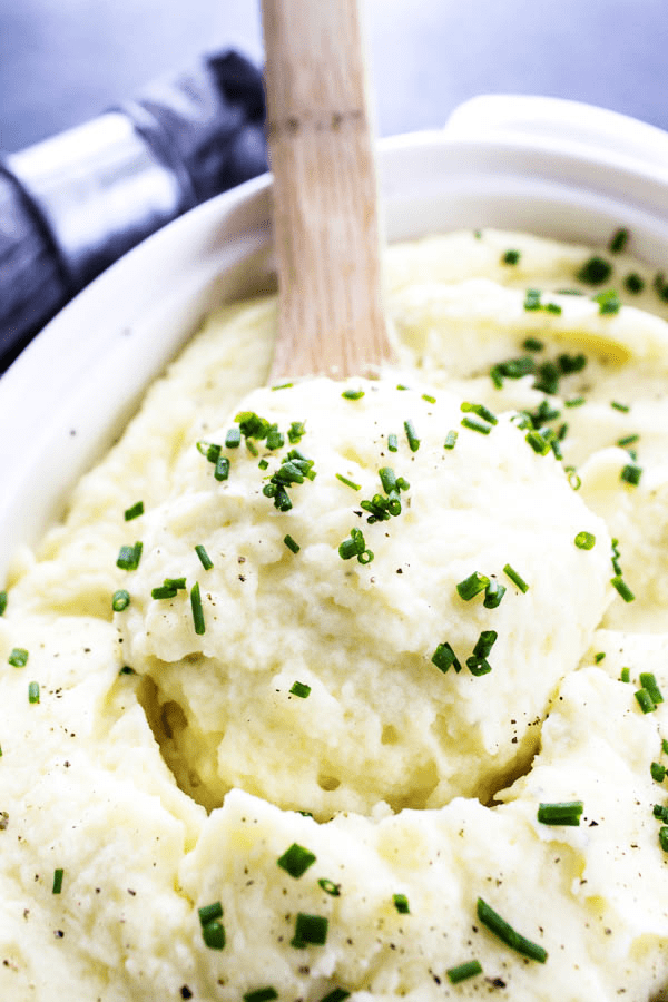 These BEST MASHED POTATOES are light and fluffy, while still rich and creamy; making these the perfect mashed potatoes for any meal or holiday. mashed potatoes topped with green onion in white serving dish with wooden spoon.