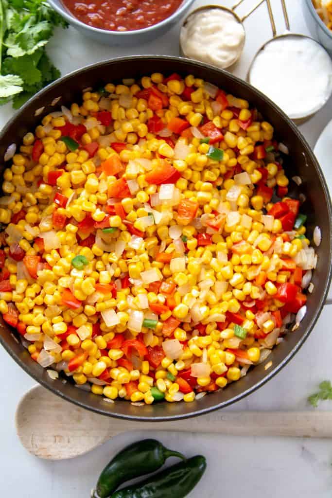 Grab a bag of chips and dig in. This Corn Queso dip is insanely cheesy, creamy & delicious. It will become your new favorite game day cheese dip. skillet filled with corn, red bell peppers, onions and jalapenos