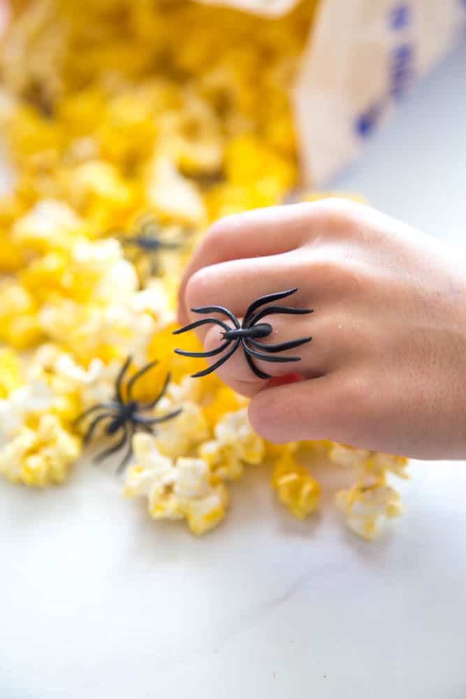 a hand grabbing popcorn with black spider ring on the ring finger